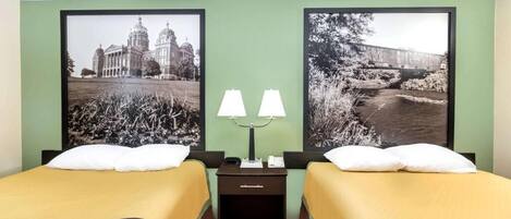 Una habitación de hotel con dos camas, una mesita de noche con lámparas y dos cuadros en la pared.
