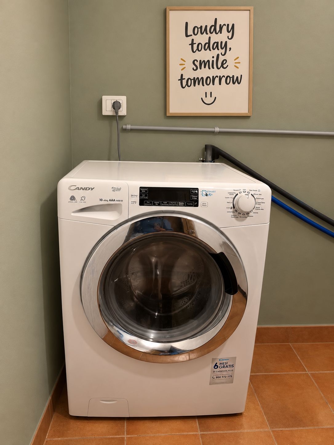 Eine weiße Waschmaschine von Candy mit Frontlader, einer an der Wand montierten Handtuchstange und einem motivierenden Spruch an der Wand.