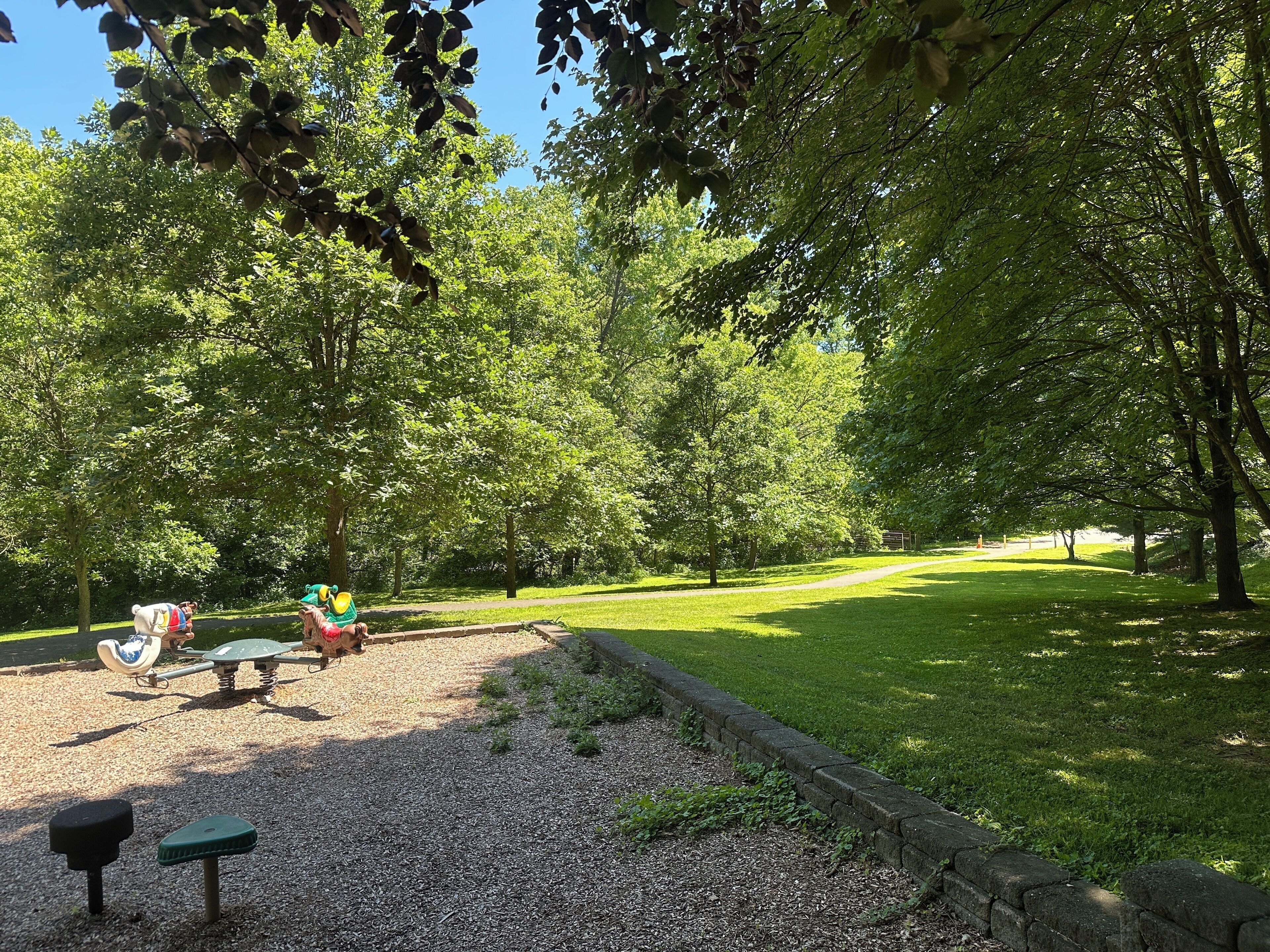 Un parque con juegos infantiles, un sendero de grava y césped verde.