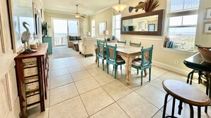 A spacious kitchen with a dining area, featuring a large island, teal chairs, and a view through the windows.