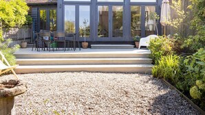 Une maison moderne dotée d’une grande porte vitrée, d’un patio avec des meubles d’extérieur et d’un jardin de gravier.