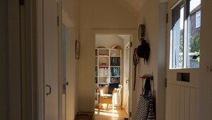 Un couloir étroit avec une bibliothèque, un fauteuil en osier et un radiateur.