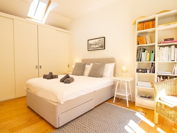 A bedroom with a bed, a bedside table with a lamp, a bookshelf, and a window with skylight. - The Studio House-Design & Garden | Pass The Keys (Rye)