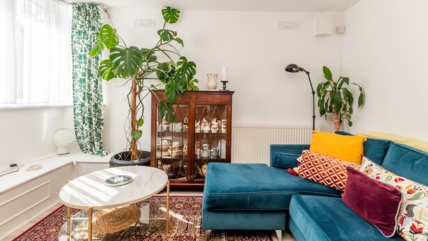 A living room with a blue sofa, a round coffee table, a cabinet with glass doors, and a large plant.