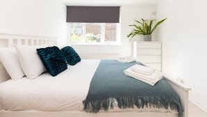A bedroom with a bed, a window with a view, a plant, and a bedside table.