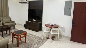 A living room with a sofa, TV, wooden cabinet, and a dining table with chairs.