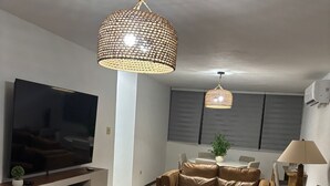 A modern living room with a flat-screen TV, leather sofas, a wooden coffee table, and two hanging pendant lights.