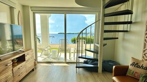 Un salon moderne doté d’un téléviseur, d’un meuble de rangement en bois et d’un escalier en colimaçon menant à un balcon offrant une vue sur la mer.