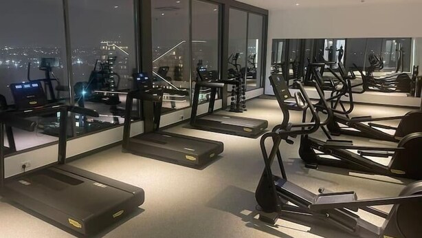 A gym with treadmills and exercise bikes, large windows with a city view, and a modern interior design. - Loxwood House (Accra)