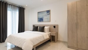 A modern bedroom with a large bed, a nightstand, a wardrobe, and a painting on the wall. - Loxwood House (Accra)