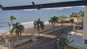 A coastal view with a beach, palm trees, and a road leading to a building with a sign that reads "Dansa". - Seafront Apartment with Pool in Martim de Sá (Caraguatatuba)