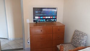 A television on a wooden dresser in a room with a patterned chair and a plain wall. - Seafront Apartment with Pool in Martim de Sá (Caraguatatuba)