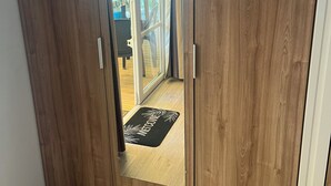 A wooden wardrobe with a sliding door, a welcome mat, and a view of an outdoor patio area. - Mobile home rental 8 berths (Parentis-en-Born)
