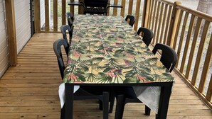 A covered outdoor deck with a table and chairs, a grill, and a view of mobile homes in the background. - Mobile home rental 8 berths (Parentis-en-Born)