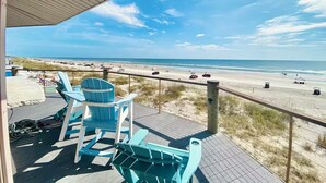 Eine Strandterrasse mit blauen Adirondack-Stühlen und Blick auf den Strand, bewölkter Himmel.