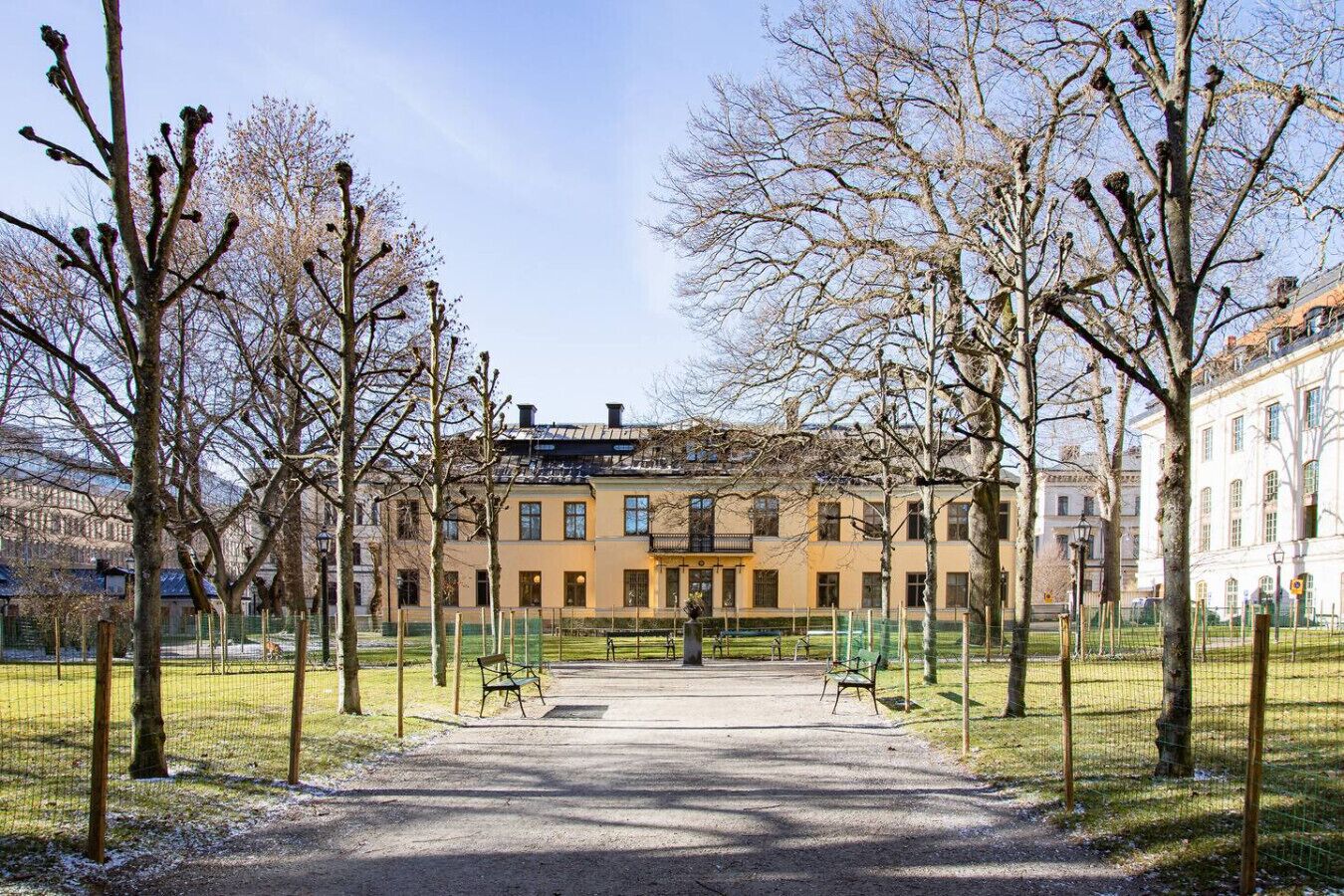 A building with a symmetrical facade, a central entrance, and a paved courtyard with benches.