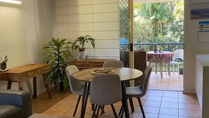 A dining area with a round table, six chairs, a wooden side table, and a potted plant. - Baden 26 - Rainbow Shores (Rainbow Beach)