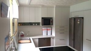 A compact kitchen with white cabinets, a microwave, a refrigerator, and a dishwasher. - Baden 26 - Rainbow Shores (Rainbow Beach)