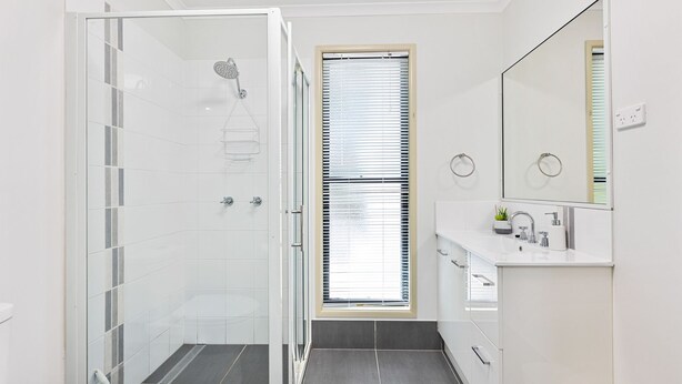 A modern bathroom with a glass shower enclosure, a window with blinds, a white sink with a mirror, and a small potted plant. - Beachcomber - Rainbow Shores (RAINBOW BEACH)
