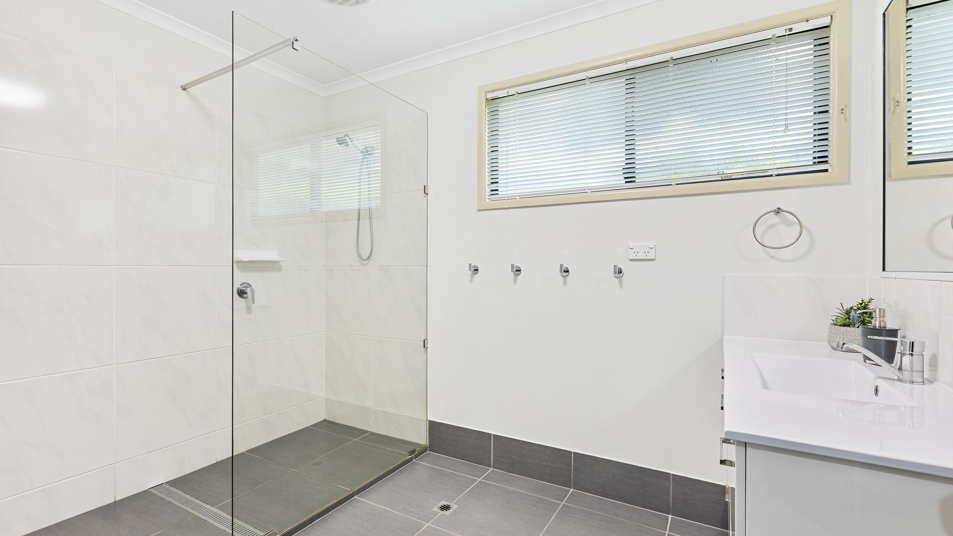 Une salle de bain moderne avec une douche à parois de verre, un lavabo avec un miroir et une fenêtre équipée de stores.
