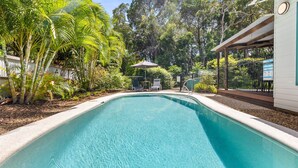A swimming pool with a surrounding garden, a covered seating area, and a fence.