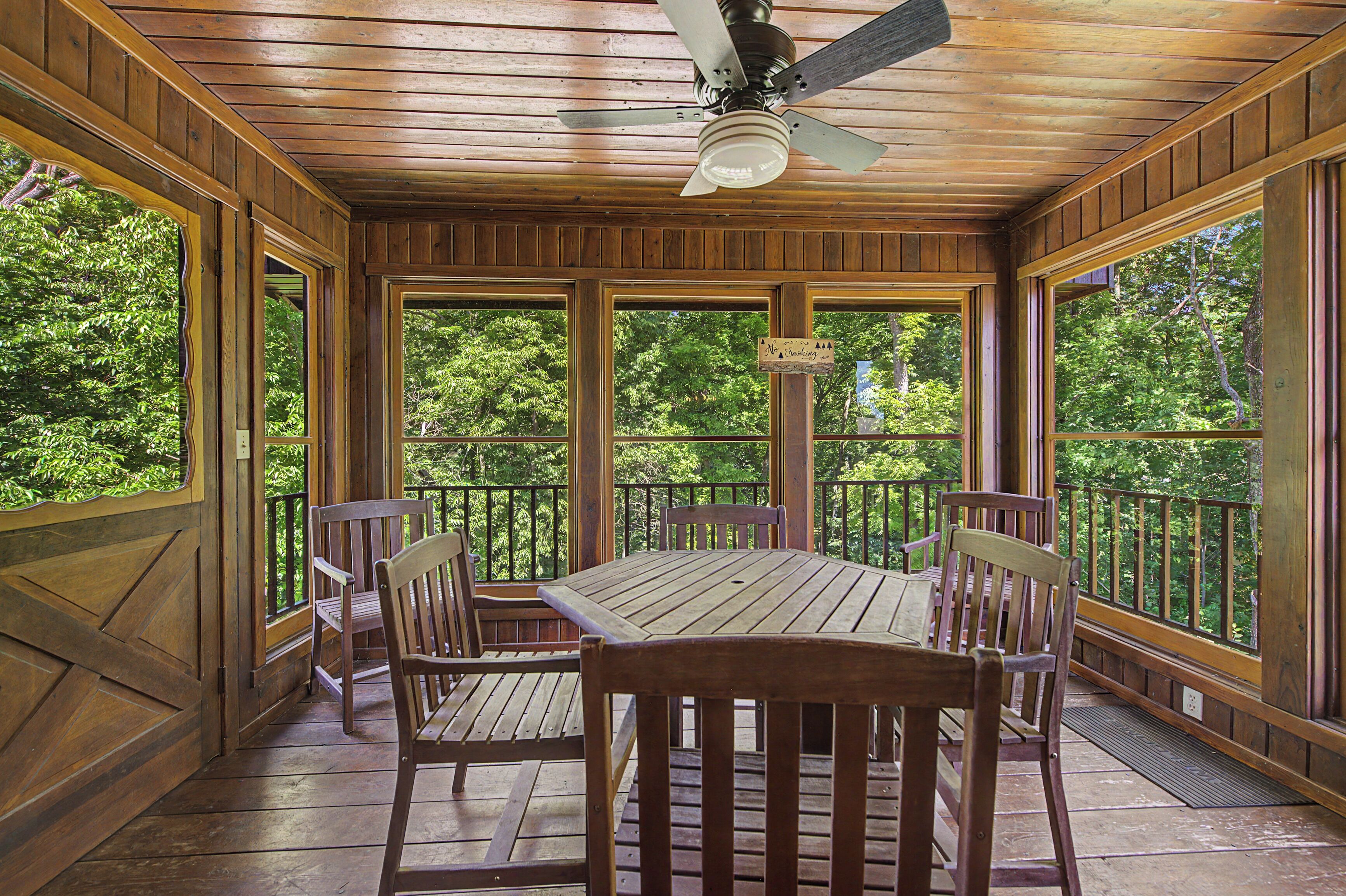 A wooden deck with a table and chairs, large windows, and a ceiling fan.