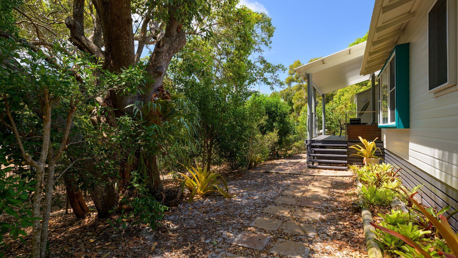 A pathway leading to a house with a porch, surrounded by dense foliage and trees.