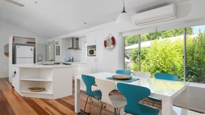 Une cuisine moderne avec des meubles blancs, un îlot central et un coin repas doté de chaises de couleur turquoise.
