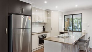 Una cocina moderna con un refrigerador de acero inoxidable, armarios blancos, un horno empotrado y un amplio ventanal con vistas a árboles.