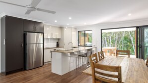 Una cocina moderna con una isla central, electrodomésticos de acero inoxidable y un comedor con mesa y sillas de madera.
