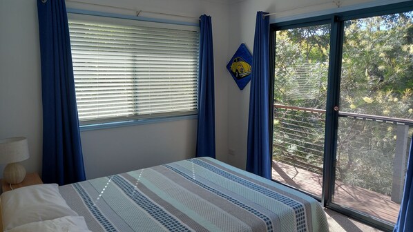 A bedroom with a bed, a window with blinds, a balcony with a railing, and a painting on the wall. - Mortimer - Rainbow Shores (Rainbow Beach)