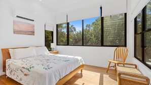 Ein Schlafzimmer mit Bett, Stuhl, Nachttisch, Fenster mit Jalousien und einem Bild an der Wand.