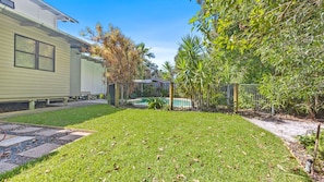 Un jardin à l’arrière d’une maison d’habitation, avec une piscine, une zone délimitée par une clôture et la maison elle-même.