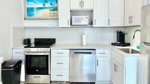 Una cocina moderna con armarios blancos, microondas, cafetera, lavavajillas y horno.