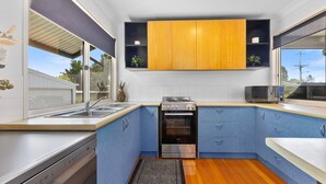 Cocina compacta con estufa, horno y lavadero, armarios de madera y ventana con vistas a zonas verdes.