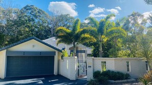 A two-story house with a garage, surrounded by a brick wall and palm trees.