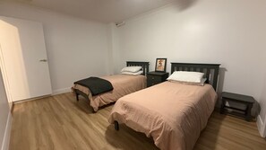 A room with two single beds, a small bedside table with a lamp, and a door.