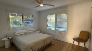 A bedroom with a bed, two bedside tables, a chair, and a ceiling fan.
