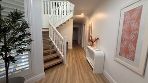 A staircase leading to an upper floor, a hallway with a wooden floor, and a wall with a framed artwork.