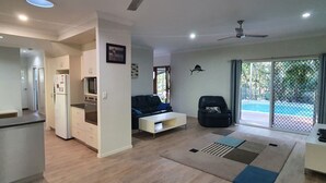 A modern living room with a sofa, a black armchair, and a dining area with a refrigerator and oven.