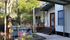 A modern house with a covered porch, a wooden door, and a small garden with various plants.