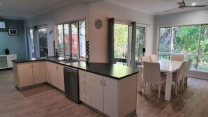 A modern kitchen with a dining area, large windows, and a ceiling fan.