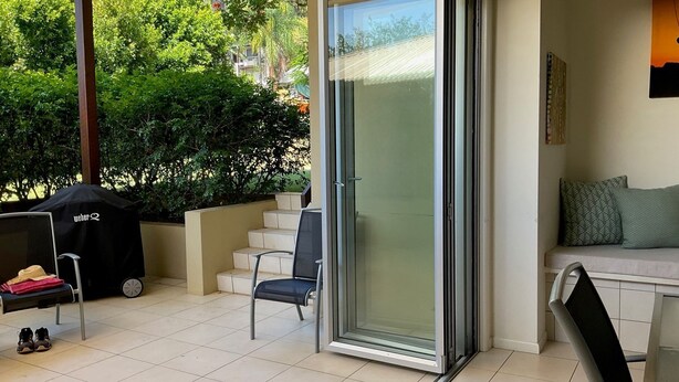 Un espace patio avec une porte-fenêtre coulissante donnant sur un jardin, un barbecue, une chaise et un canapé.