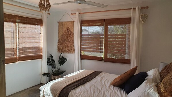 A bedroom with a bed, a ceiling fan, and a window with a woven blind.