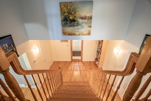 A wooden staircase with a painting above it, a door at the bottom, and a light fixture on the wall.