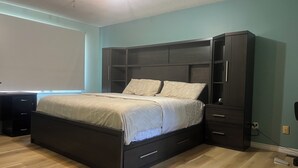 A bedroom with a bed, dark wooden wardrobe, and a desk.