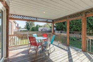 A covered patio with a wooden deck, a table with chairs, and a view of a residential area.