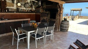 Cocina exterior con parrilla, mesa y sillas.