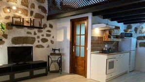 Un espacio habitable pequeño con pared de piedra, puerta de madera, kitchenette, televisor y mesa de centro.