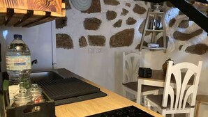 Una cocina con pared de piedra, techo de madera y sillas blancas.